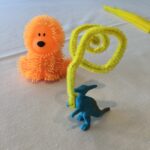 Fidgets in action. Dinosaur holding pipe cleaner, orange dog in background