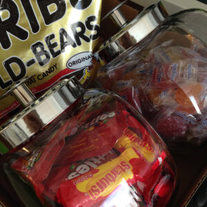 Clear glass jars filled with Starburst, fruit candy, and a bag of Haribo gummi bears behind